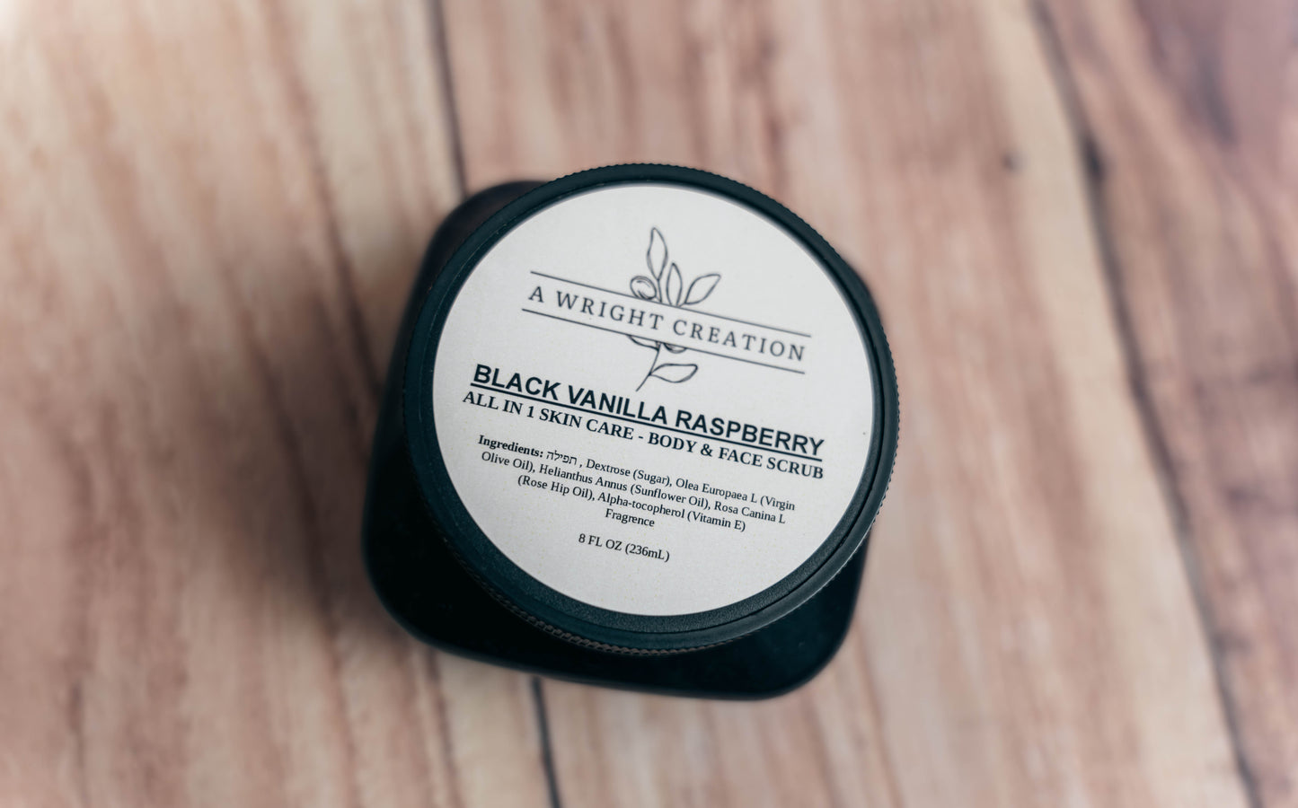 Black container of 'Black Vanilla Raspberry' scrub on a wooden surface