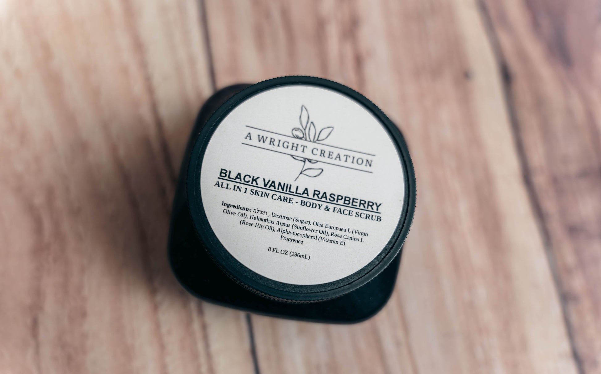 Black container of 'Black Vanilla Raspberry' scrub on a wooden surface