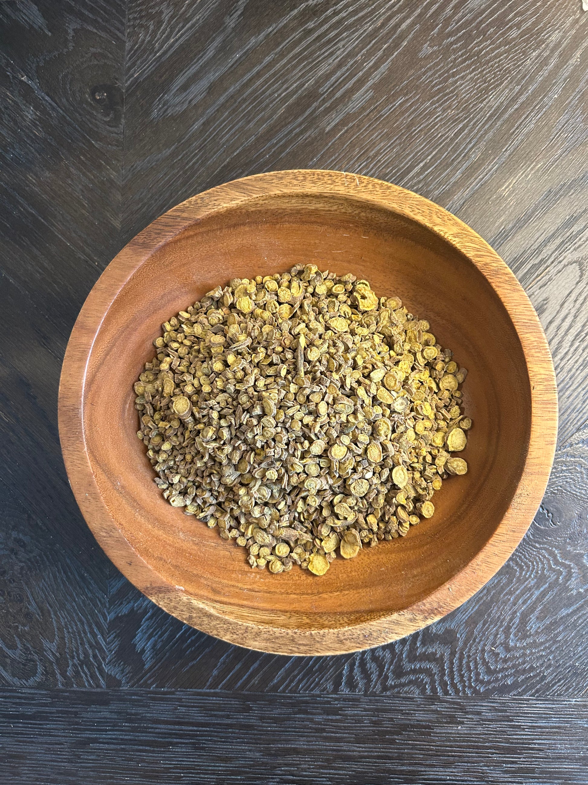 A wooden bowl filled with Wright Way whole yellow and white Organic Chamomile Flowers.