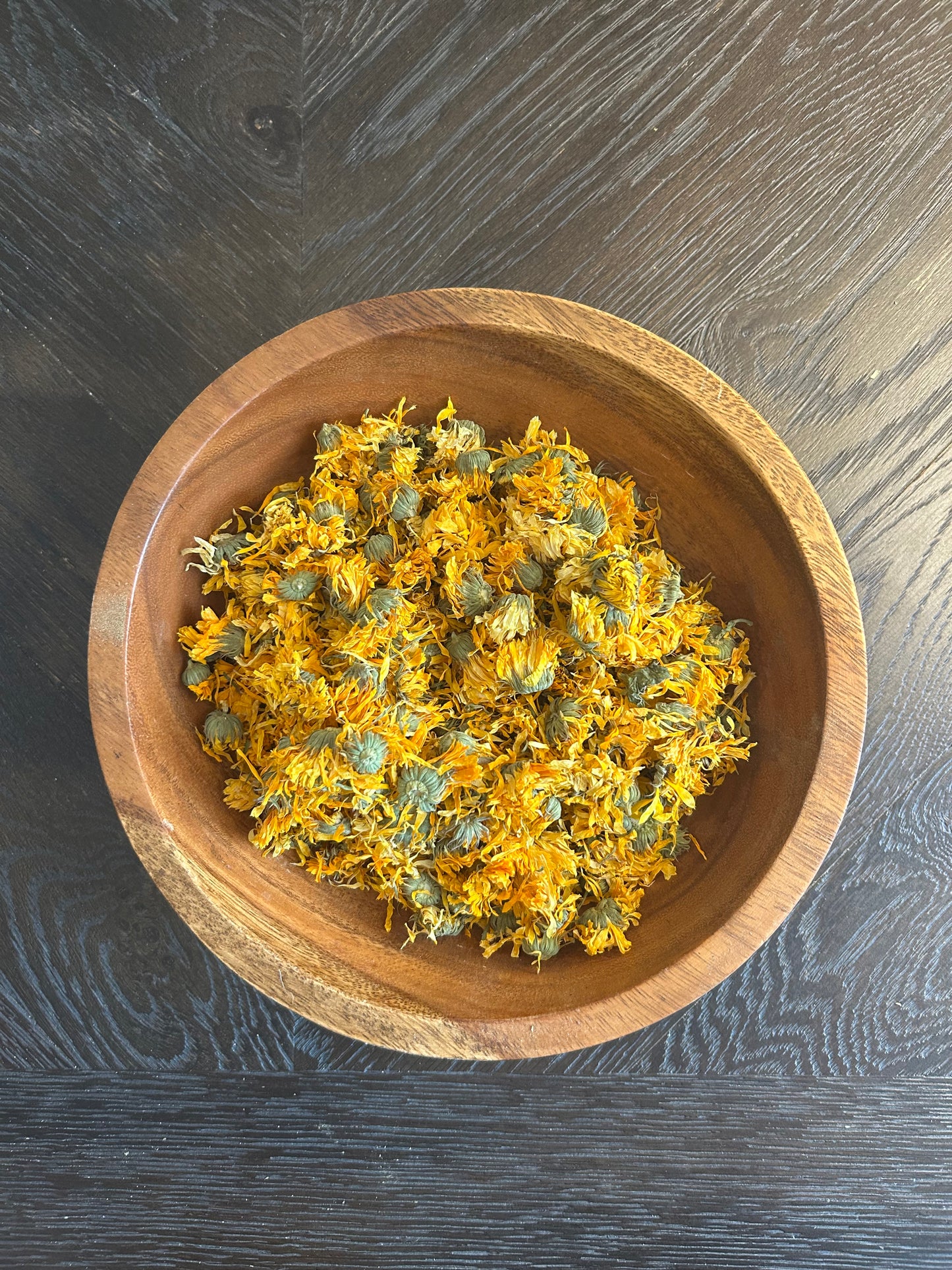 A wooden bowl of Wright Way Organic Calendula Flowers showing vibrant golden dried petals.