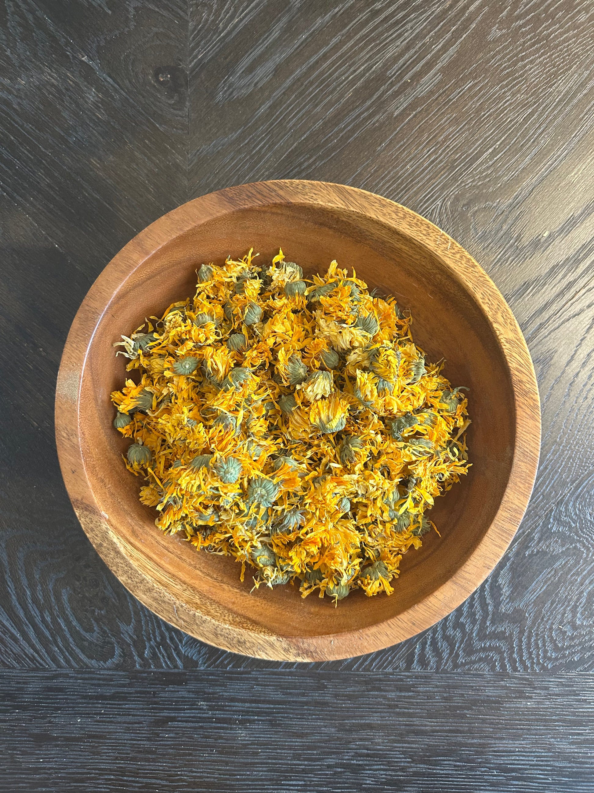 A wooden bowl of Wright Way Organic Calendula Flowers showing vibrant golden dried petals.