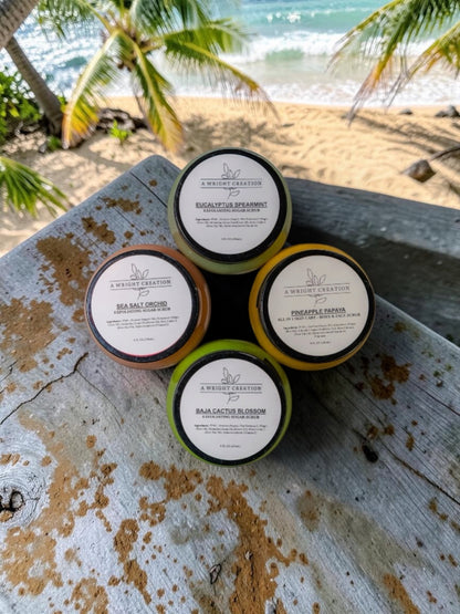 Five small containers with labels on a rustic surface near a beach with palm trees.