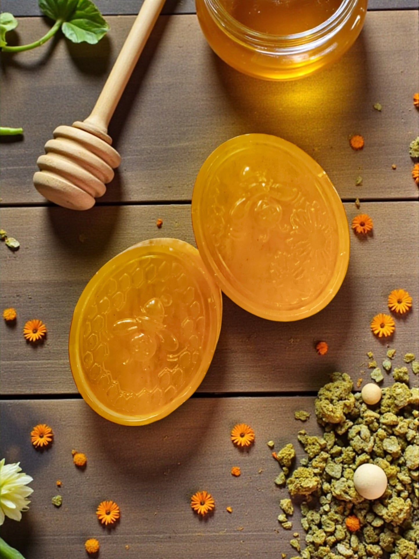 Two yellow honeycombs with a wooden honey dipper on a wooden surface with flowers and herbs.